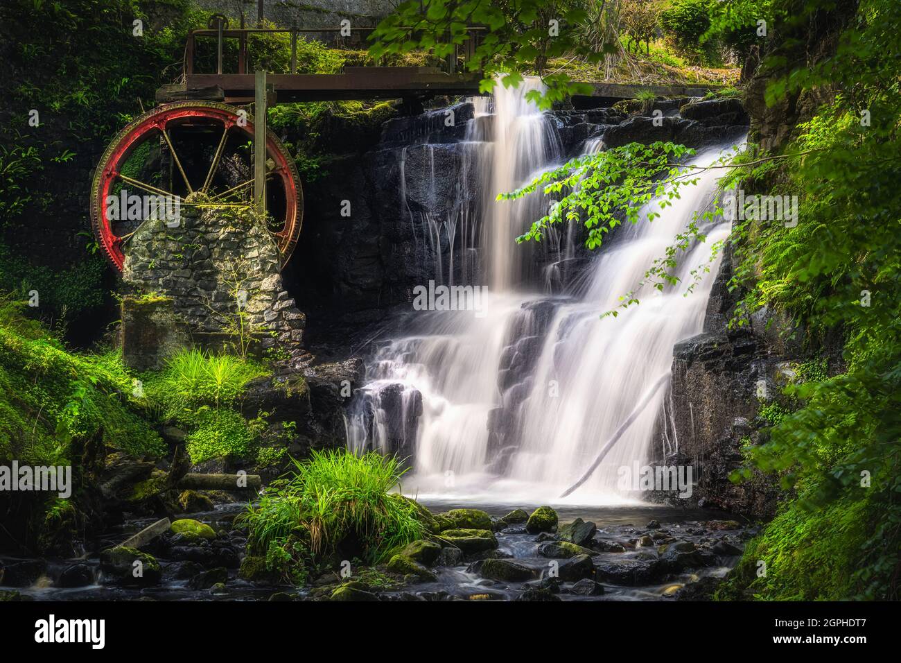 Ruota d'acqua rossa d'epoca con cascata in primavera nel Glenareff Forest Park, County Antrim, Irlanda del Nord. Foto a lunga esposizione e messa a fuoco morbida Foto Stock