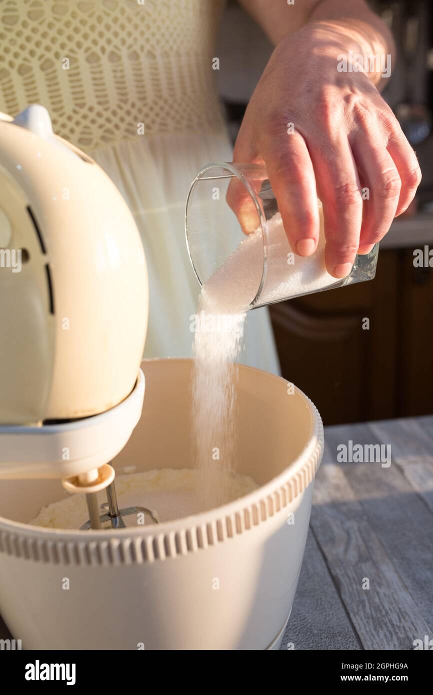 Passo dopo passo il processo di produzione della panna acida. Le mani delle donne aggiungono lo zucchero al recipiente del mixer con la panna acida. Foto Stock
