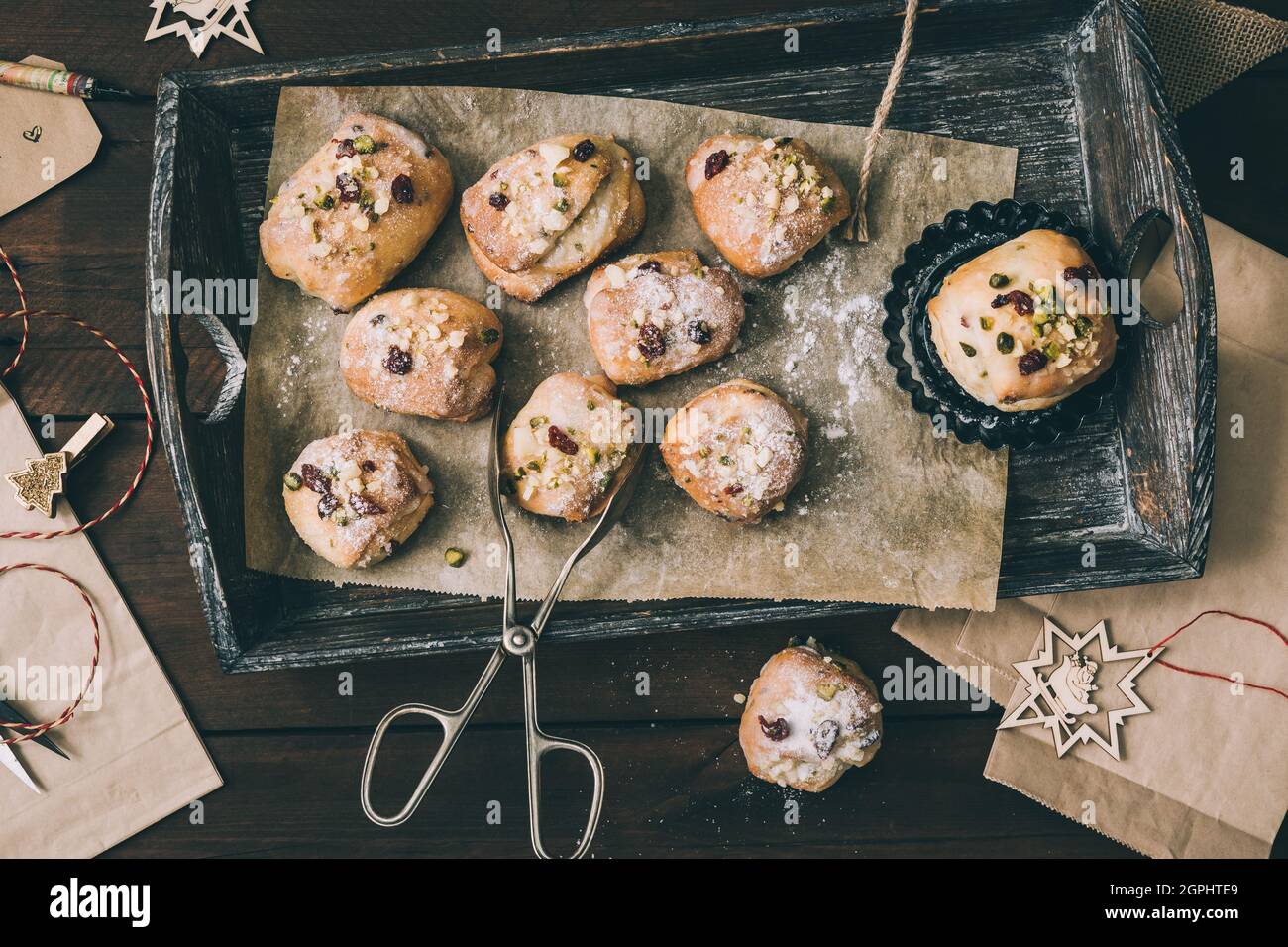 Mini Stollen con glassa di zucchero su un vassoio di legno, sacchetti di carta, forbici e nastro regalo su legno scuro, scena per preparare i regali di Natale o dell'avvento, parte superiore Foto Stock