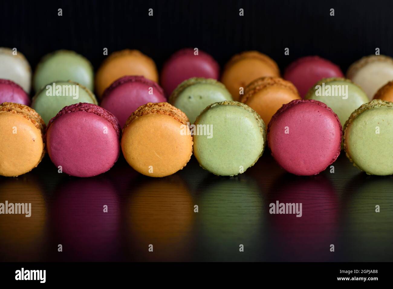 Macaron o amaretti francesi un biscotto da dessert a base di meringa e mandorla riflesso su un tavolo nero Foto Stock