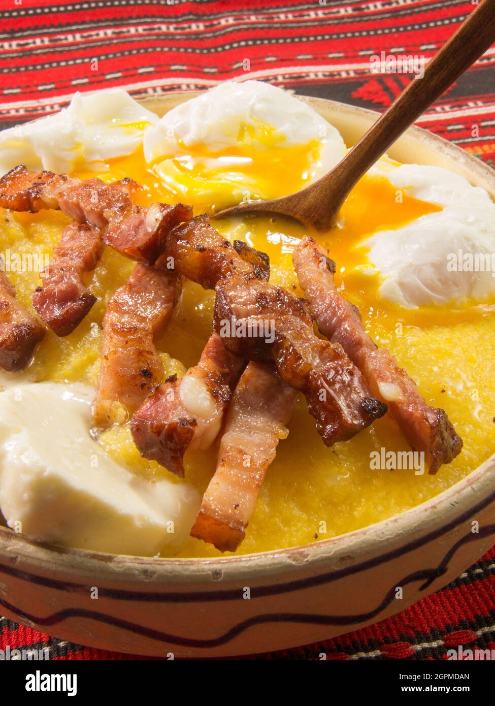 Polenta bulz con pancetta fritta e uova e cucchiaio di legno Foto Stock