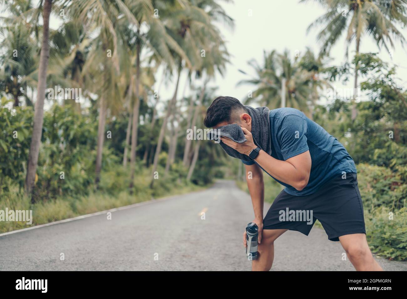 uomo sportivo che riposa dopo una corsa e strofinare il sudore con un asciugamano e una bottiglia d'acqua. sport e allenamento concetto. Foto Stock