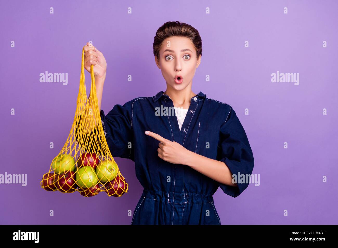 Foto di giovane scioccato stupito bella ragazza pubblicizzare raccomandare sacco di rete di riciclo isolato su sfondo di colore viola Foto Stock