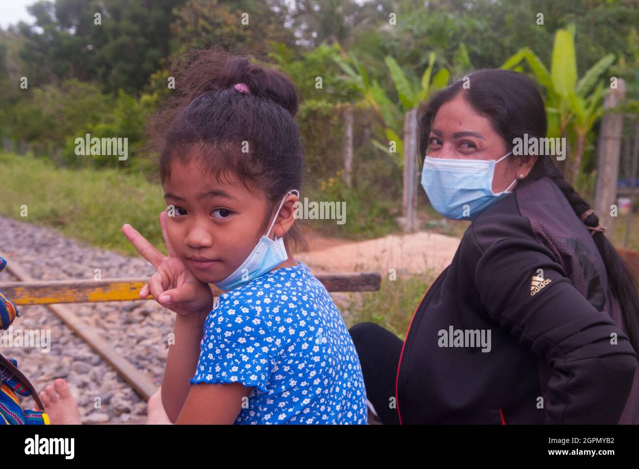 Una madre e una figlia cambogiane, entrambe dotate di maschere protettive, cavalcano il Bamboo Train durante la pandemia del COVID - 19. Provincia di Battambang, Cambogia. 24 settembre 2021. © Kraig Lieb Foto Stock