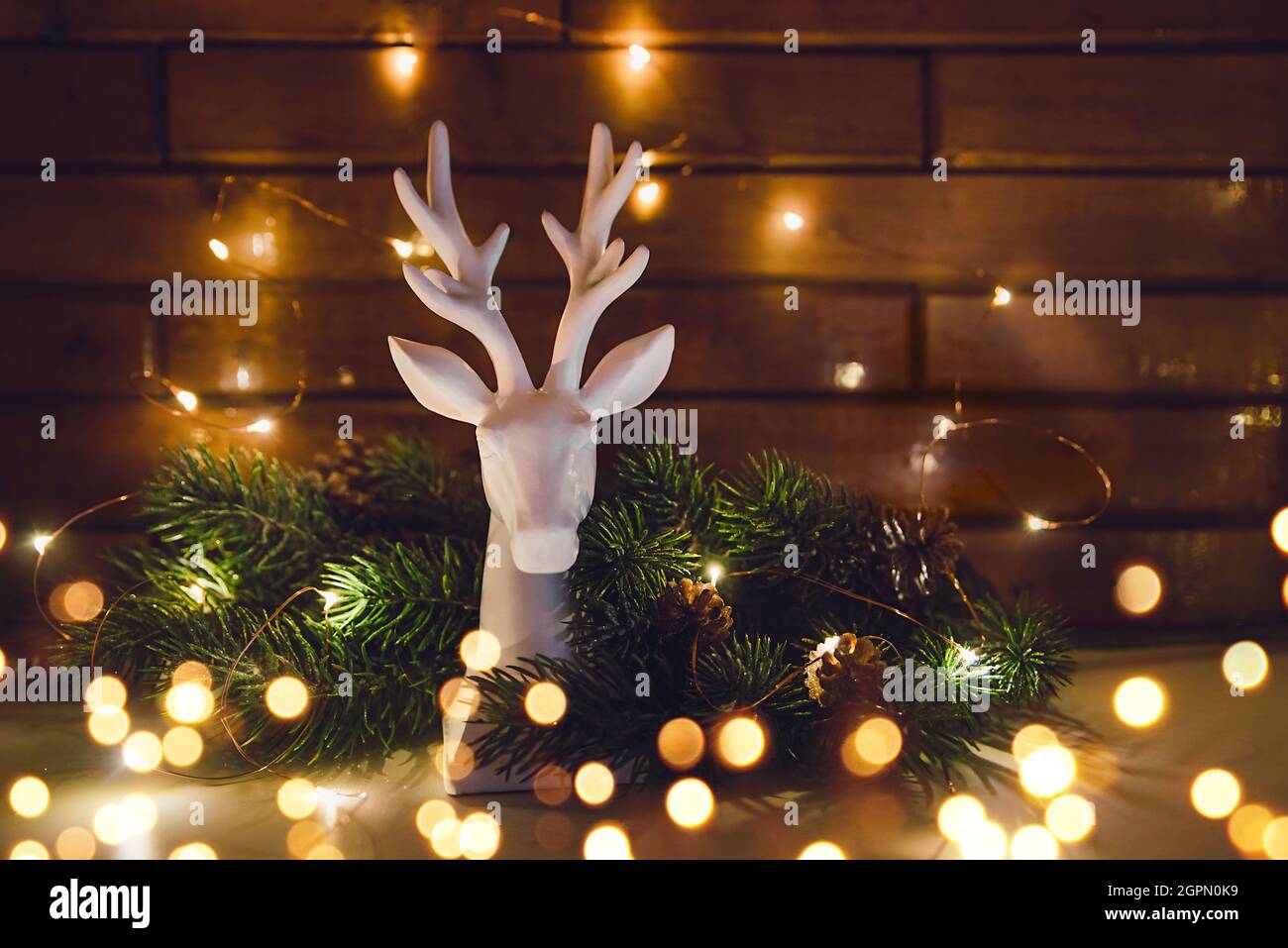 Statuina di renna con albero di Natale e ghirlanda incandescente il giorno di Natale primo piano, bokeh, in una chiave scura Foto Stock