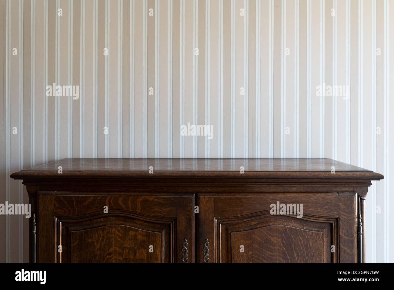vista frontale primo piano del cassetto vintage nero vuoto armadietto di legno contro una parete bianca con strisce beige Foto Stock