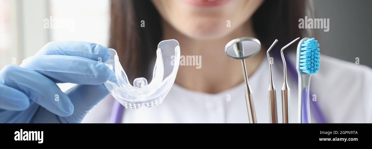 Sorridente dottore femmina tiene in mano una protezione in plastica trasparente per la bocca e strumenti stomatologici Foto Stock