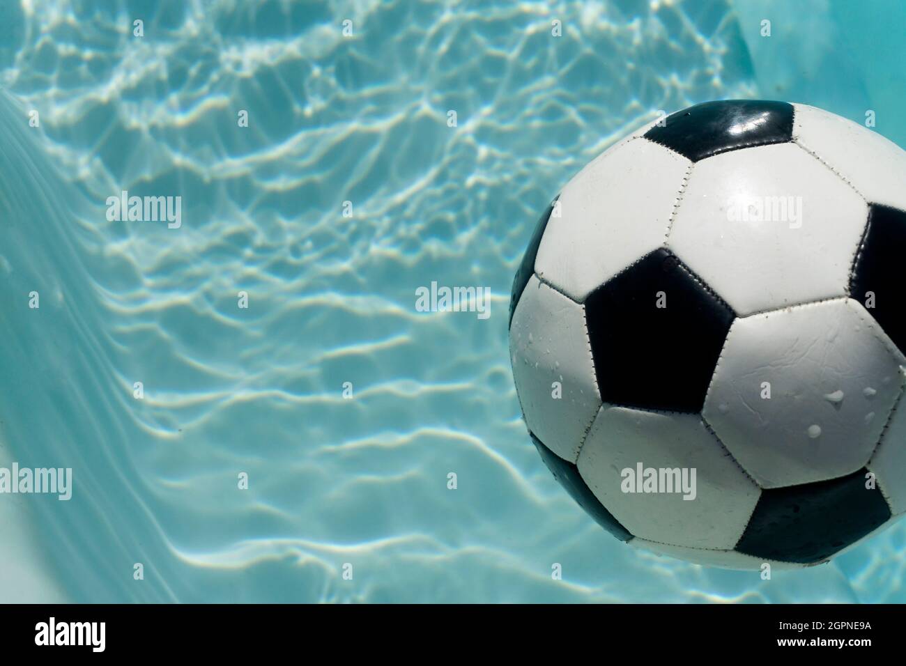 Calcetto bianco e nero galleggiante in una piscina blu chiaro. Sfondo sportivo estivo Foto Stock
