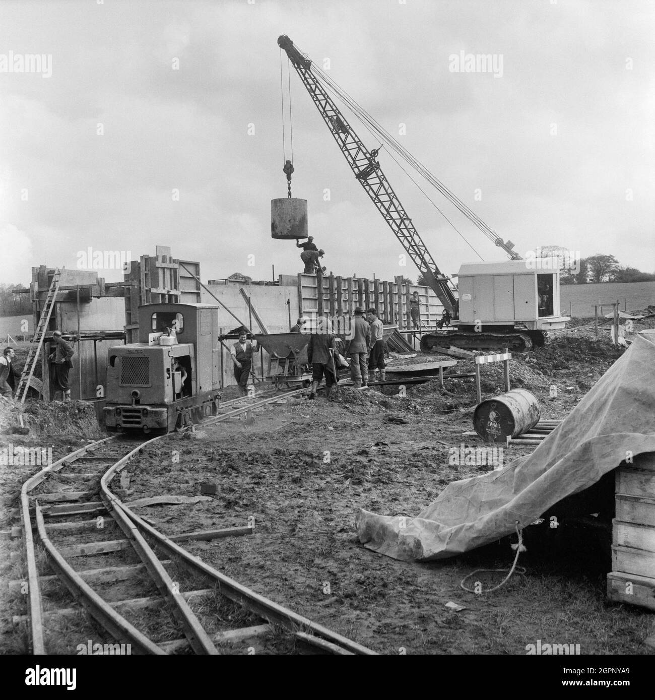 Una vista della costruzione di una struttura, probabilmente sulla sezione B dell'autostrada Birmingham-Preston (M6), che mostra un motore su una ferrovia a scartamento ridotto, una gru e un gruppo di lavoratori che svolgono vari compiti. Nei registri per la raccolta, l'oggetto della fotografia è stato registrato come "servizi di riparazione per il posto B.1. M6'. I lavori sull'autostrada da Birmingham a Preston (M6), tra gli svincoli da J13 a J16 iniziarono nel giugno 1960 e furono eseguiti da John Laing Construction Ltd. La sezione B era lunga 6 1/2 miglia tra Whitgreave e Beech. Foto Stock