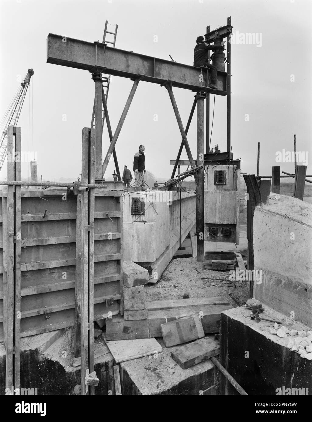 Una vista della costruzione dell'autostrada Birmingham-Preston (M6), che mostra un lavoratore che guarda un altro lavoratore che regola i martinetti da 200 tonnellate in preparazione per abbassare la trave sul Ponte 332. Questa immagine è stata catalogata come parte del Breaking New Ground Project in collaborazione con il John Laing Charitable Trust nel 2019-20. Foto Stock