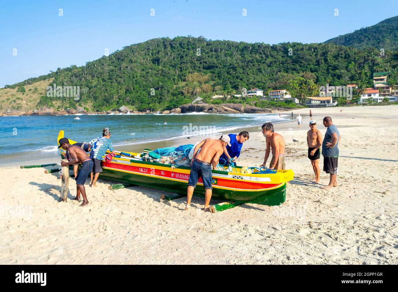 Persone della comunità e altri partecipanti che si preparano a spingere una nuova canoa artigianale da pesca in mare. L'inaugurazione di una canoa è un tradit Foto Stock