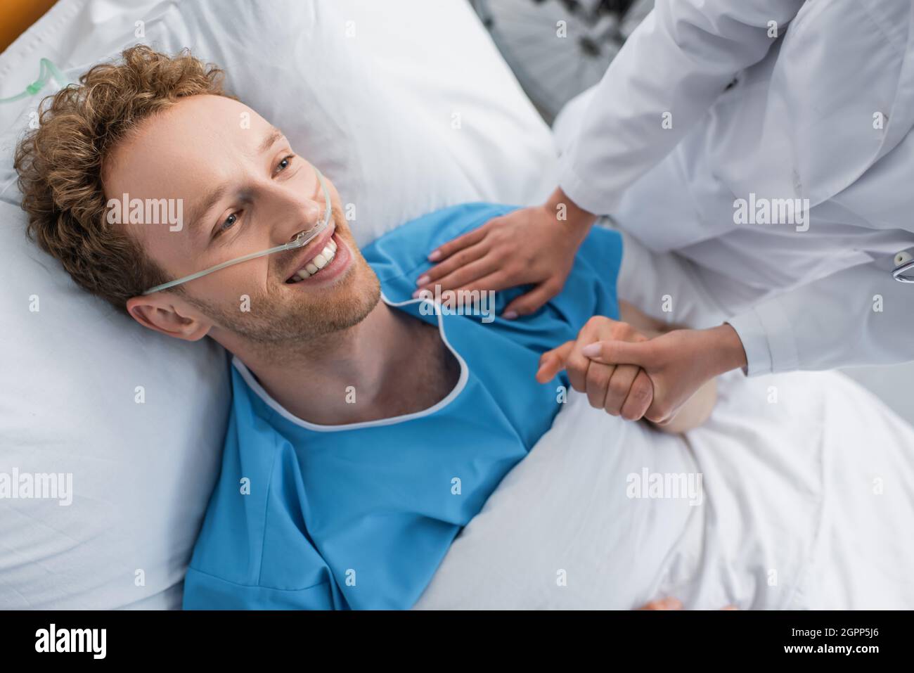 vista ad angolo elevato della mano di sostegno del medico del paziente sorridente con cannula nasale Foto Stock