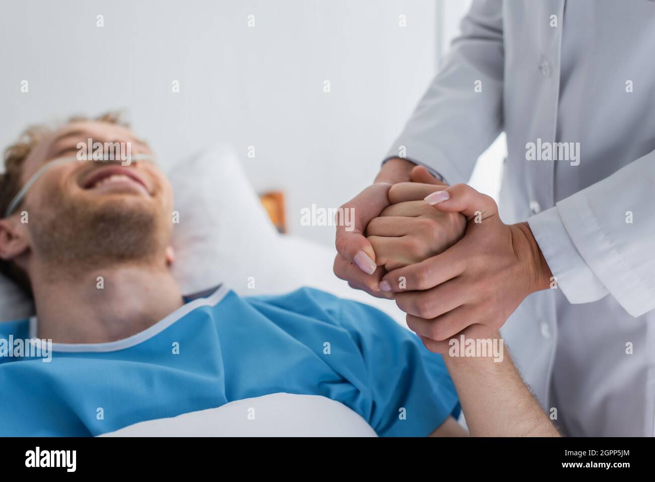 medico che tiene la mano di un paziente sfocato e sorridente con cannula nasale Foto Stock