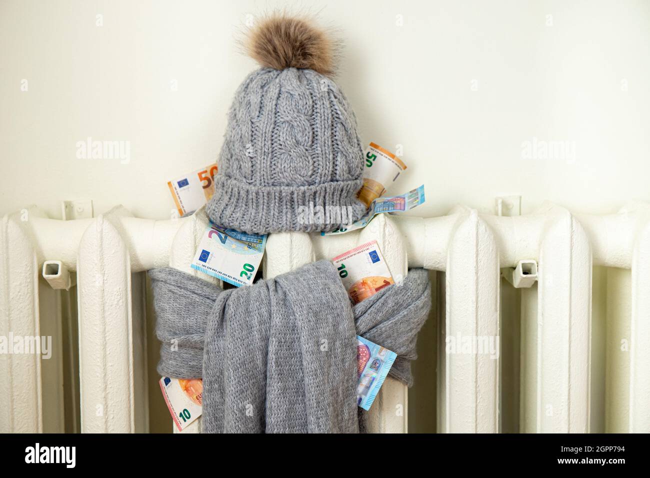 Radiatore di riscaldamento vintage con cappello invernale e sciarpa ripieni di euro. La bolletta dell'elettricità aumenta, concetto europeo di crisi energetica. Foto Stock