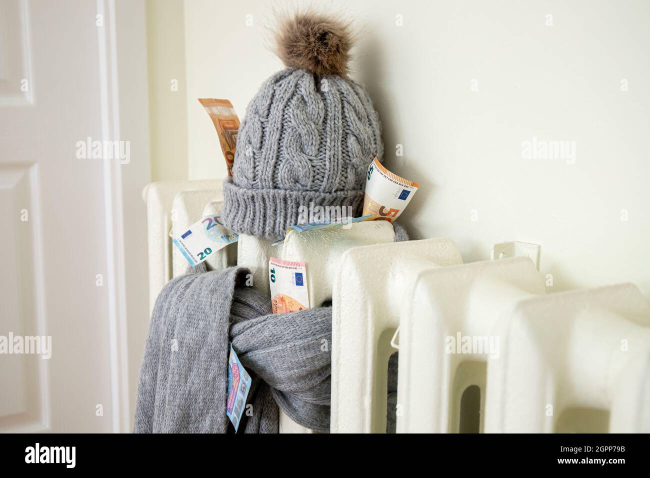 Radiatore di riscaldamento vintage con cappello invernale e sciarpa ripieni di euro. La bolletta dell'elettricità aumenta, concetto europeo di crisi energetica. Foto Stock