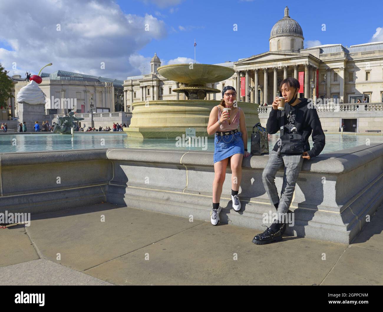 Londra, Inghilterra, Regno Unito. Due giovani bevono caffè da asporto a Trafalgar Square Foto Stock