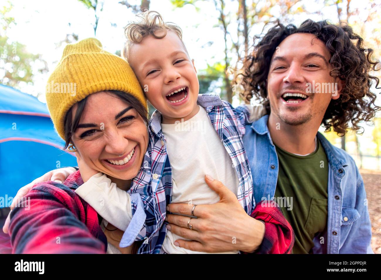 giovane felice famiglia ritratto campeggio all'aperto con tenda in autunno natura. mamma, papà e bambino piccolo fare un selfie pov nel selvaggio. persone che si divertono Foto Stock