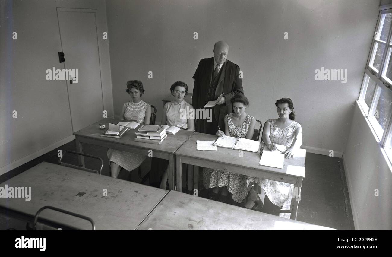 anni '50, storica, quattro giovani donne che indossano i vestiti  dell'epoca, abiti floreali, seduti a due scrivanie in legno in una piccola  aula con il loro lavoro universitario. In un vestito e