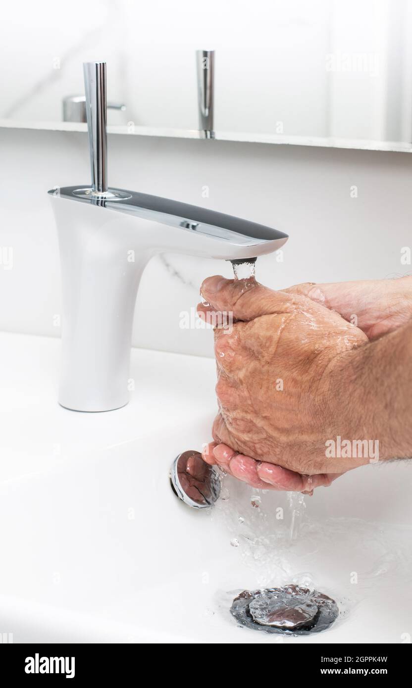 Lavando le mani con acqua nel rubinetto del progettista in un lavandino bianco Foto Stock