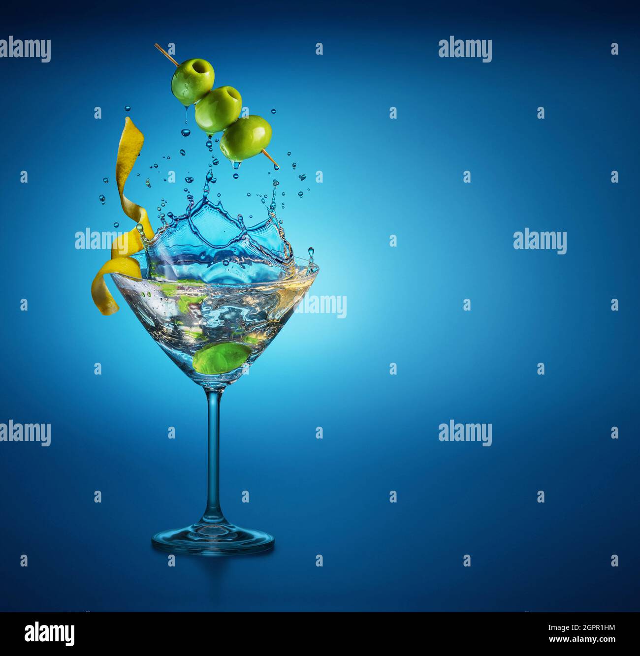 Bicchiere Martini con un incredibile spruzzi a causa della caduta di bacche d'oliva in esso. Sfondo blu. Foto Stock