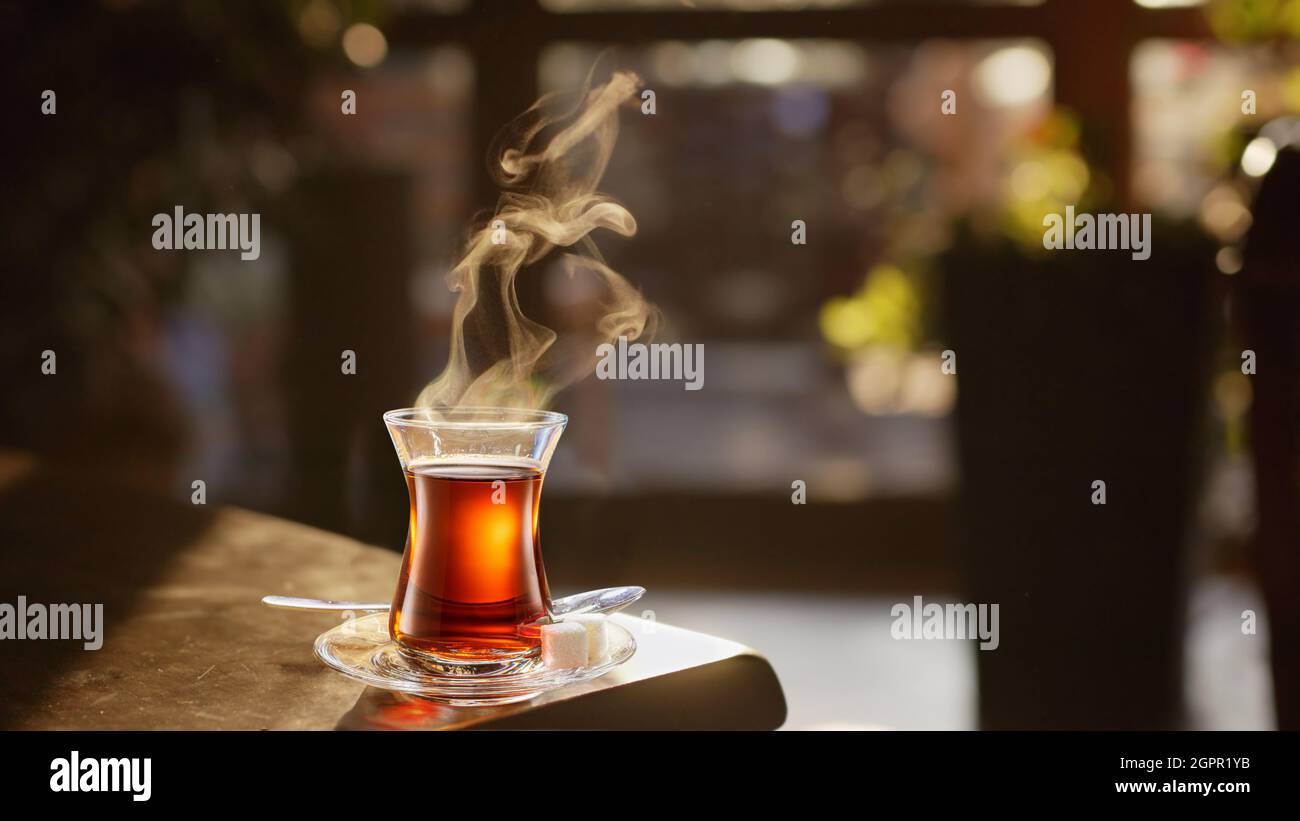 Tè turco al vapore servito in vetro a forma di tulipano su una piccola pentola sul tavolo di legno. Foto Stock