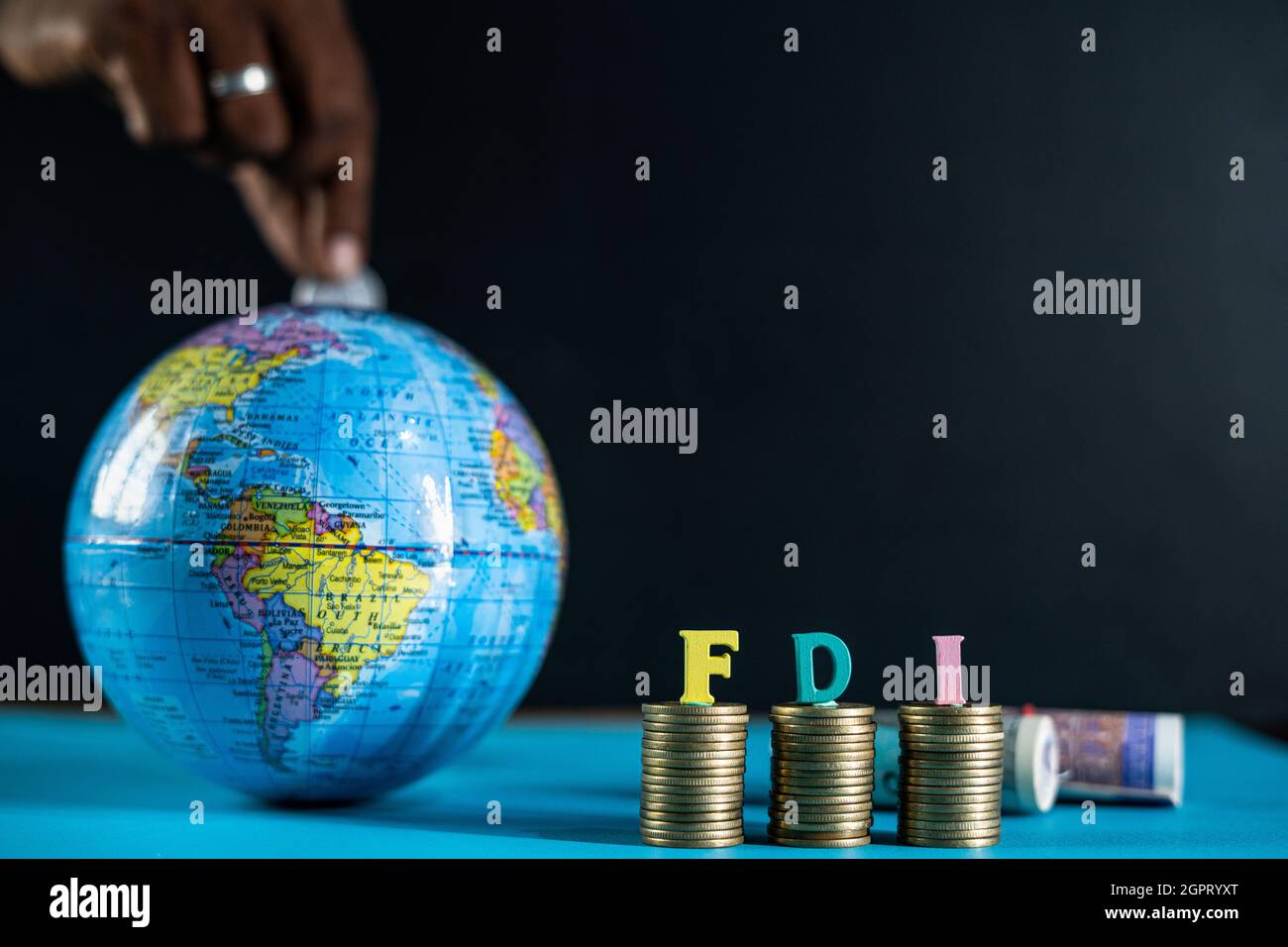 Focus sulle lettere di FDI sulle monete, concetto di FDI o investimenti diretti esteri, mostrando collocando monete all'interno del globo da dietro. Foto Stock
