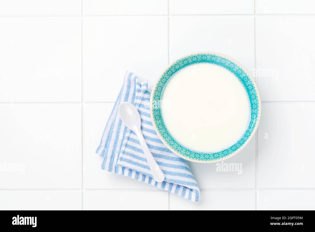 Yogurt greco in ciotola blu, tovagliolo di lino e cucchiaio di legno su tavola bianca. Vista dall'alto Foto Stock