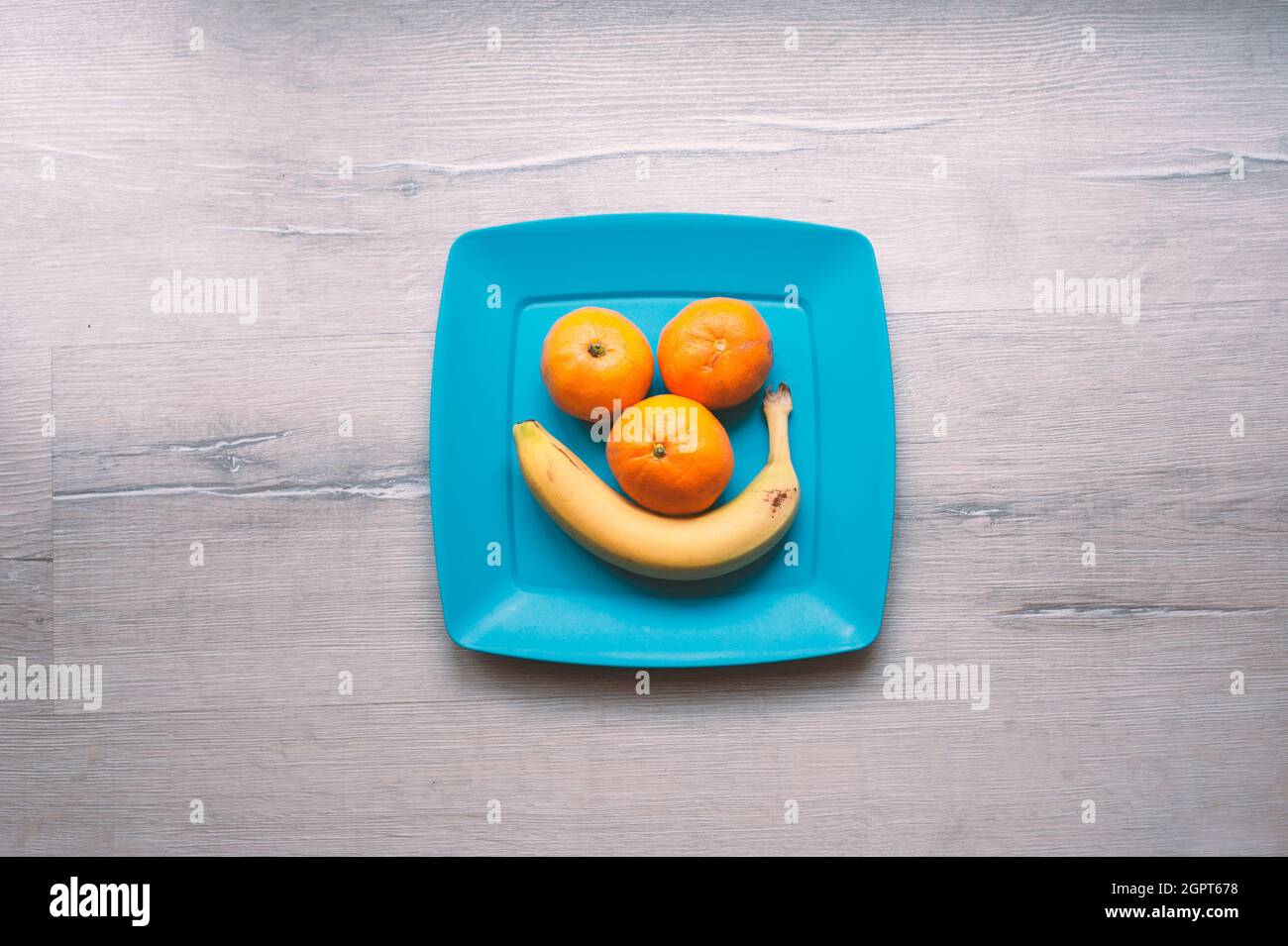 Tre tangerini e una banana su un piatto blu Foto Stock