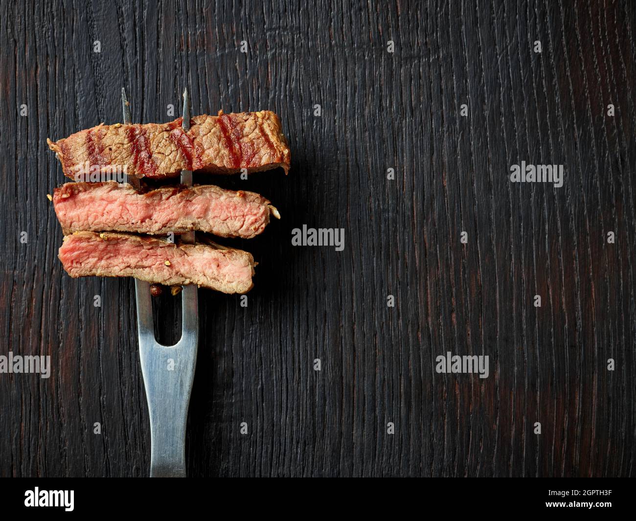 Fette di bistecca di manzo su forchetta di carne su un tavolo di legno, vista dall'alto Foto Stock