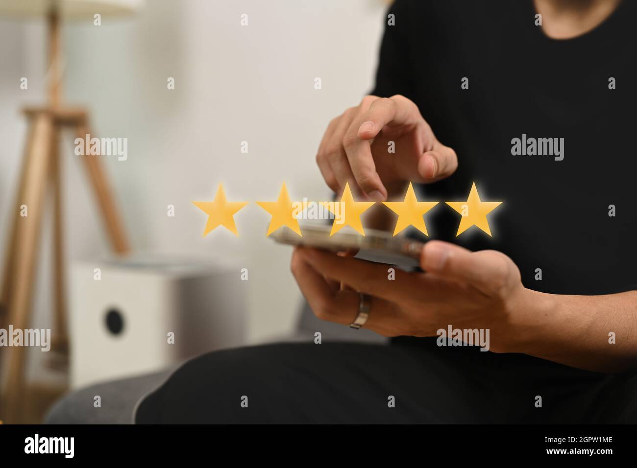 Giovane uomo che preme sullo schermo dello smartphone dando un feedback positivo con cinque stelle d'oro. Foto Stock