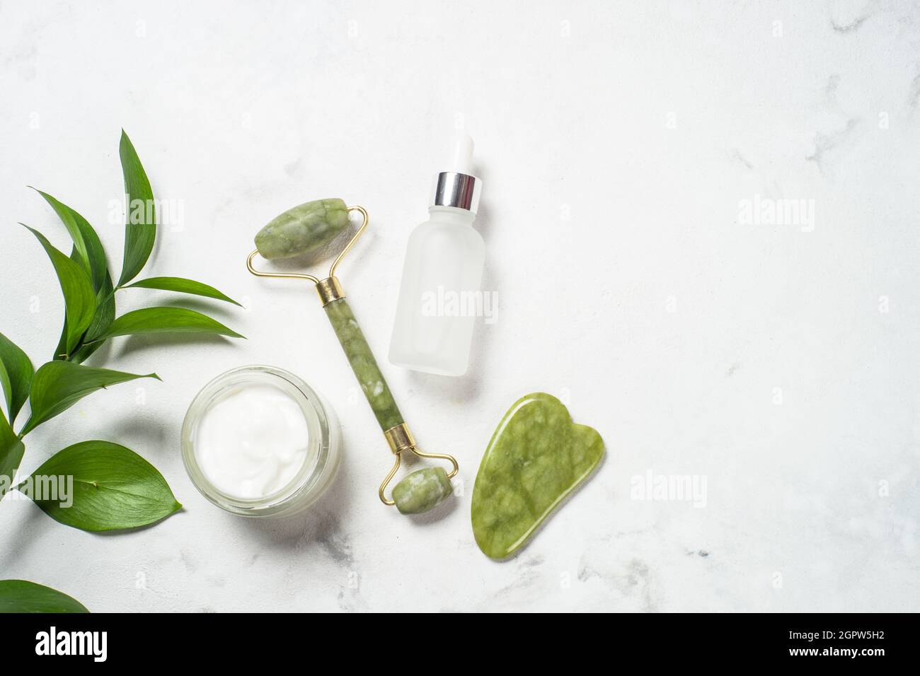 Massaggiatore Jade Roller e pietra gua sha con crema per il viso e bottiglia di siero. Foto Stock