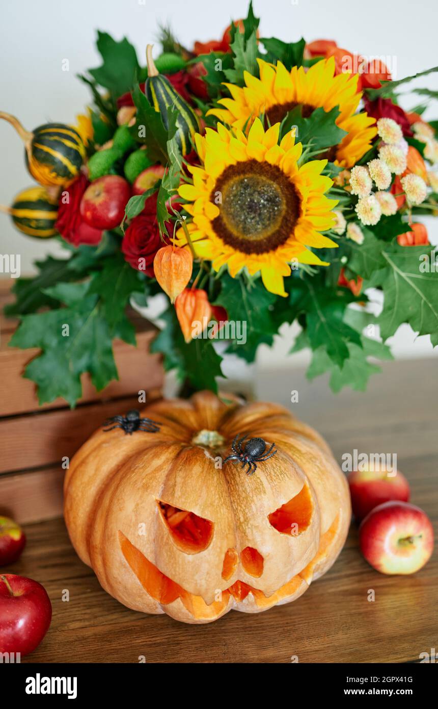 Concetto autunnale: Zucche, candele, girasole, ragni e altri attributi al tavolo come sfondo tema Halloween partito. Zucca d'arancia di Halloween con faccia spaventosa malvagia. Foto verticale di alta qualità Foto Stock