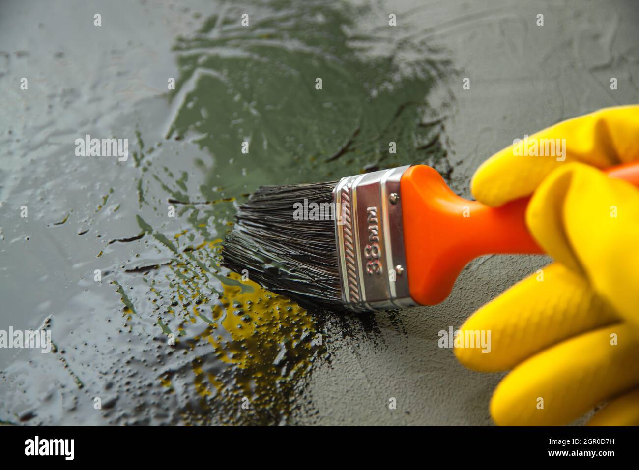 Mano primo piano in un guanto di gomma giallo con Un pennello, verniciare  la superficie di calcestruzzo con vernice nera Foto stock - Alamy