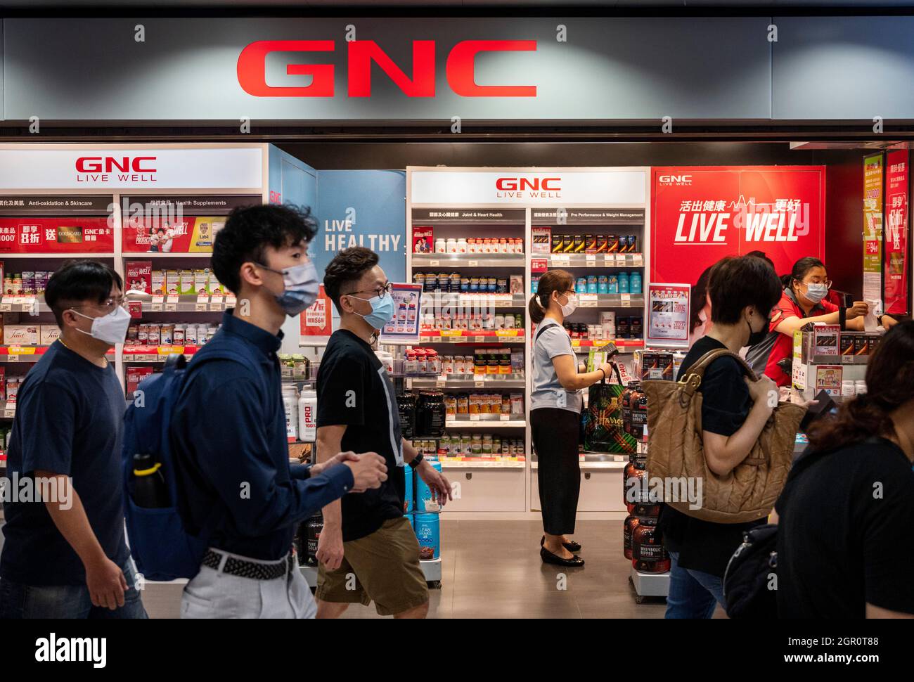 I pedoni camminano oltre i prodotti di marca relativi alla salute e alla nutrizione, il deposito dei centri generali di nutrizione (GNC) visto a Hong Kong. Foto Stock