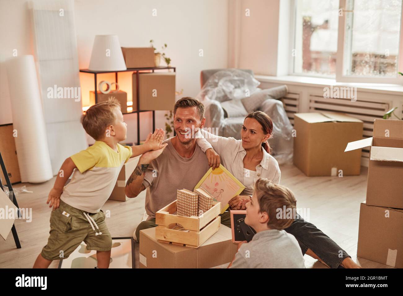 Ritratto di famiglia felice con due figli disimballaggio scatole mentre festeggia il passaggio in nuova casa, spazio copia Foto Stock