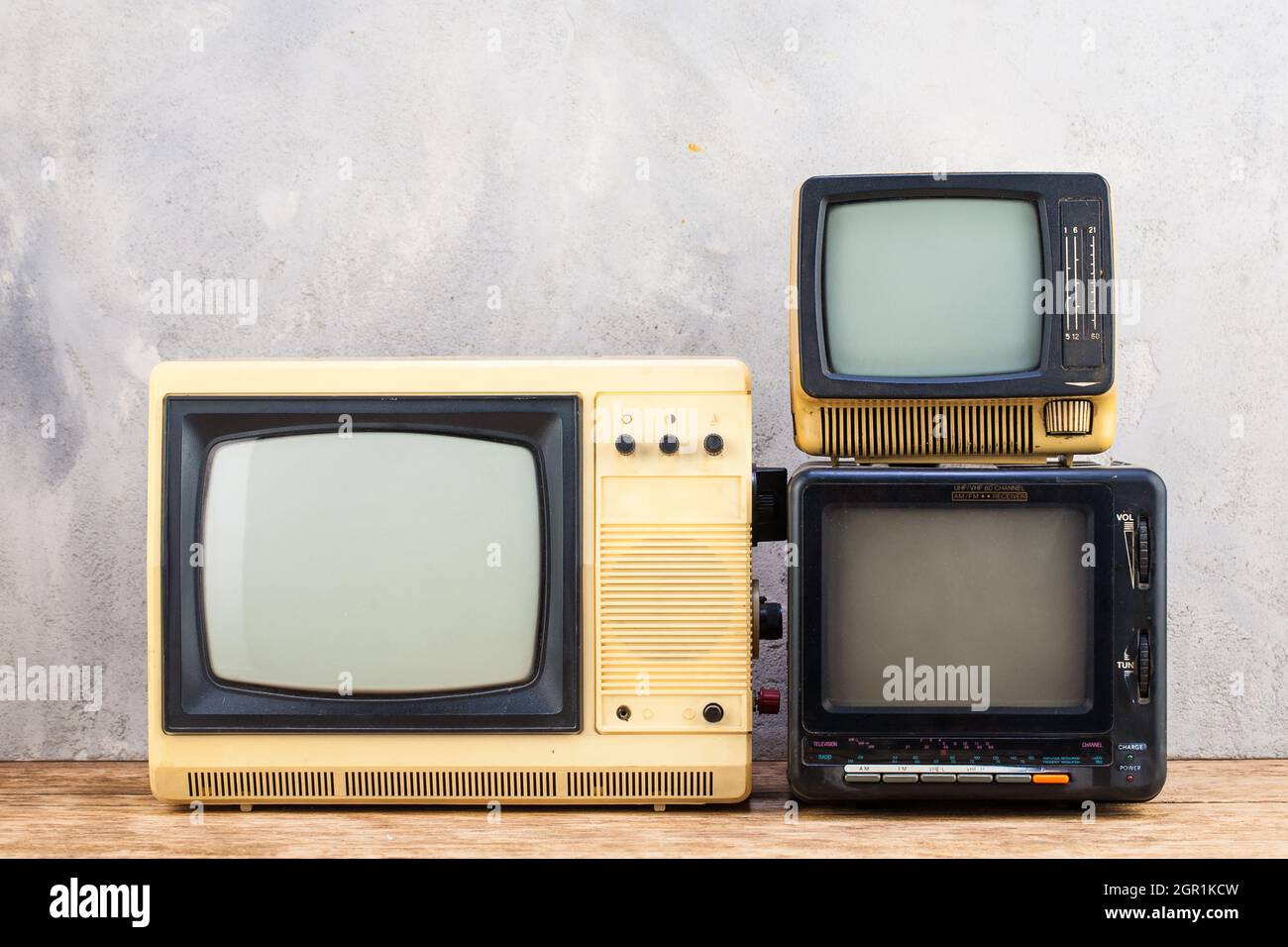 Vecchio retro analogico piccoli TV set stand su pavimento in legno fronte grigio cemento parete sfondo. Foto Stock