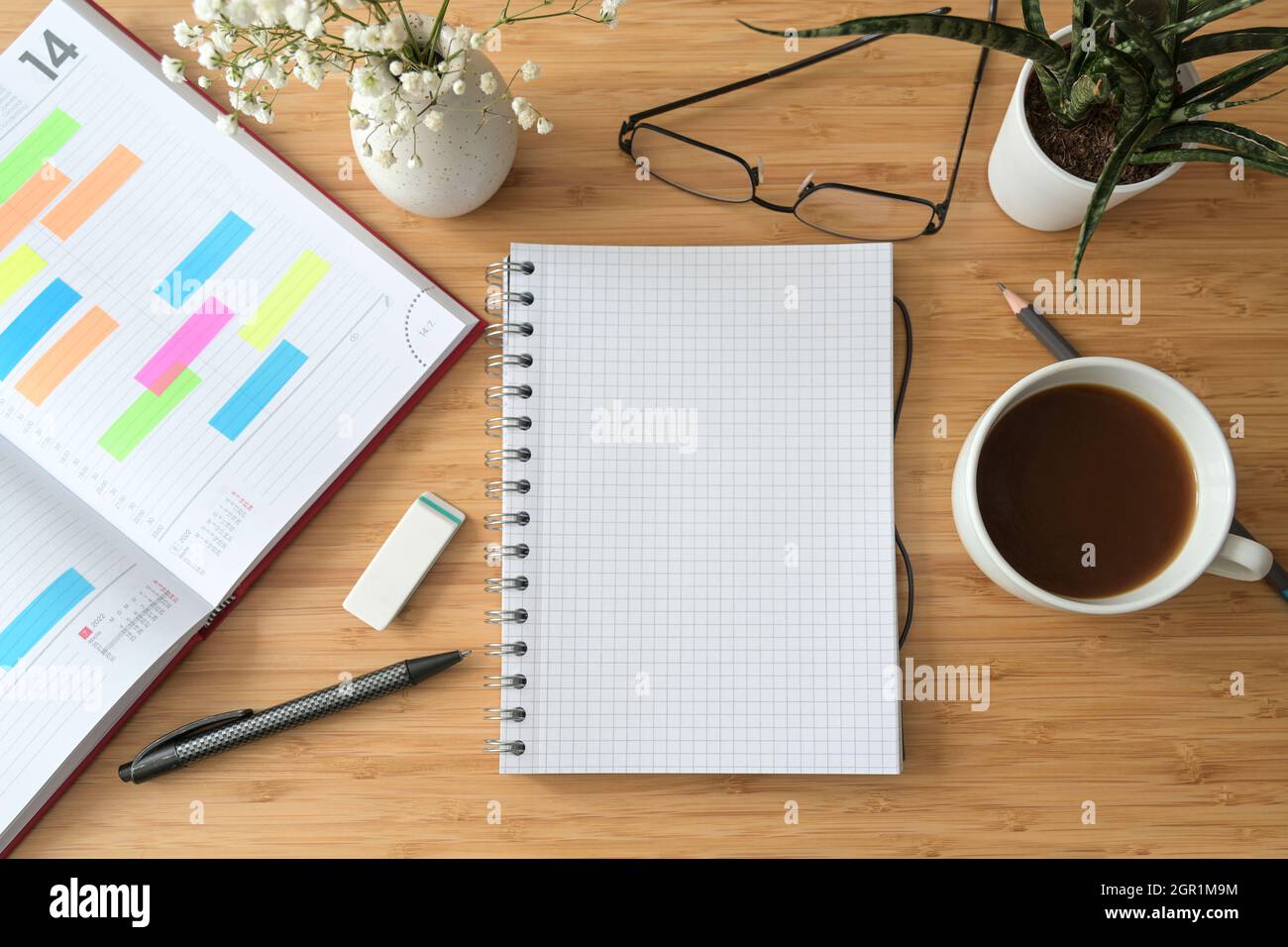 Notebook bianco a spirale su una scrivania in legno con organizer, caffè, bicchieri e fiori, spazio copia, disposizione piatta vista dall'alto, fuoco selezionato Foto Stock