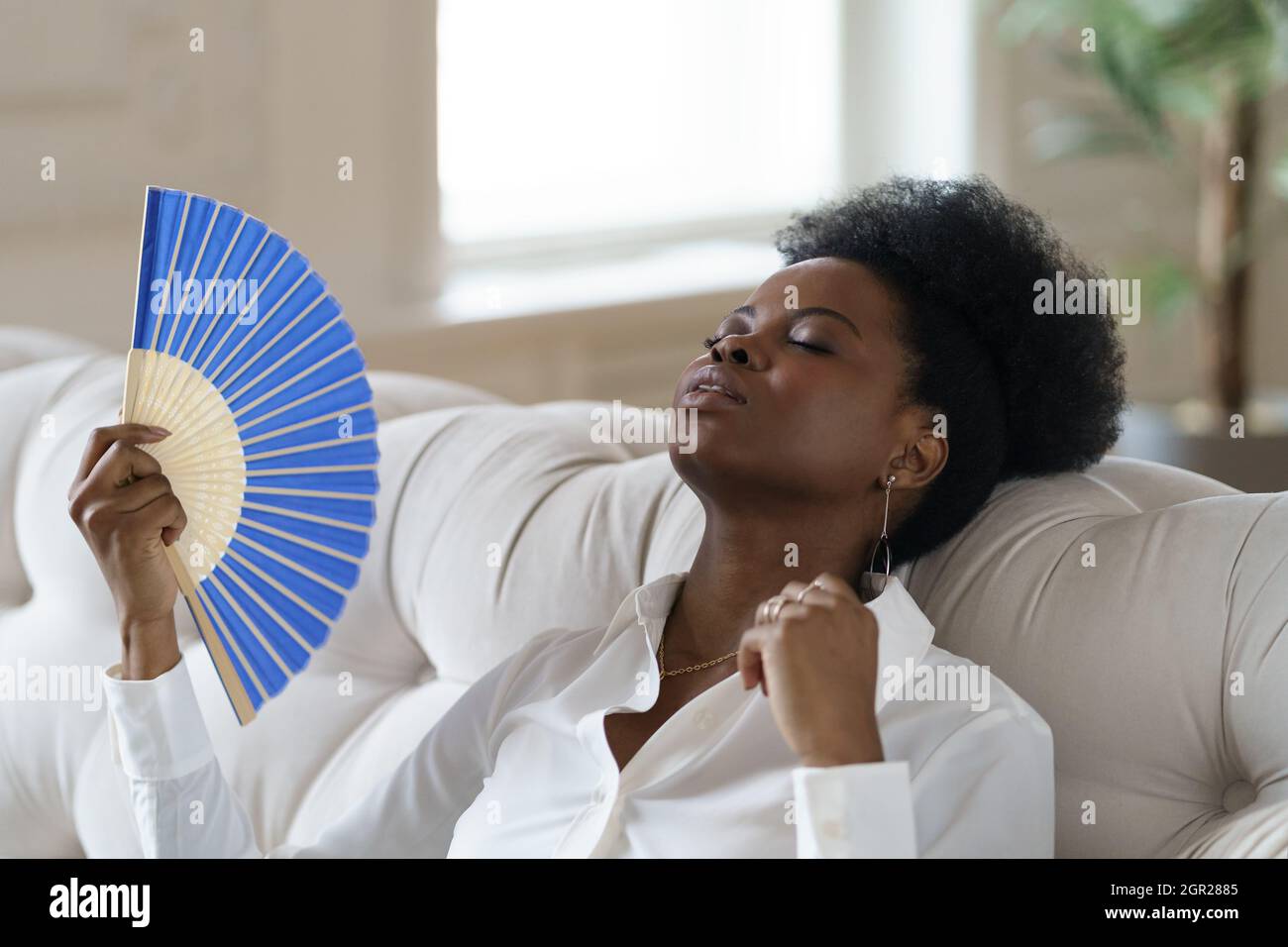 Donna che usa il ventilatore a mano mentre si rilassa sul divano a casa  Foto stock - Alamy