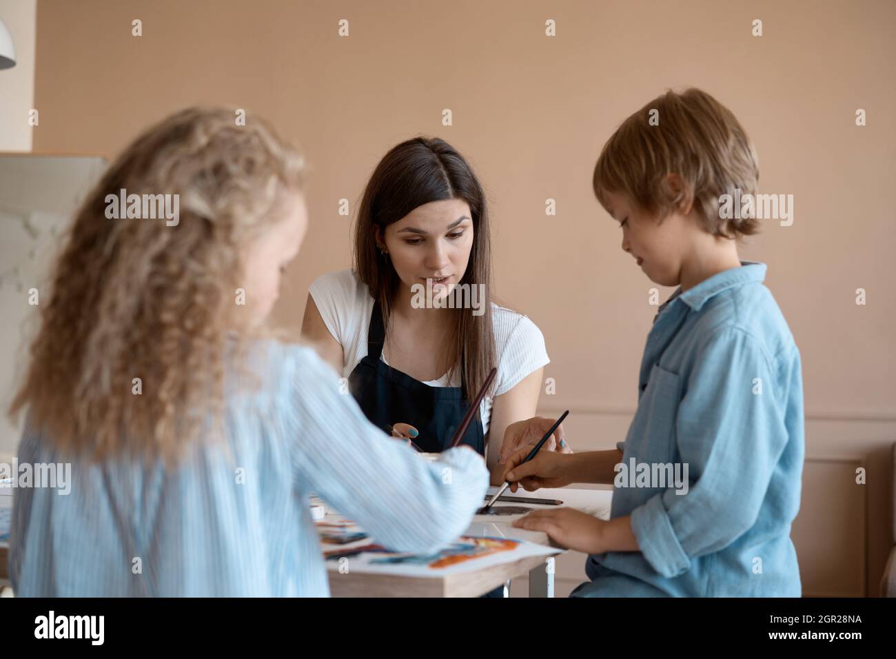 Gruppo di bambini e il loro insegnante appoggiati sul tavolo con vernici acquerello e pittura di oggetti di argilla self-made. Bambini con insegnante in classe d'arte Foto Stock