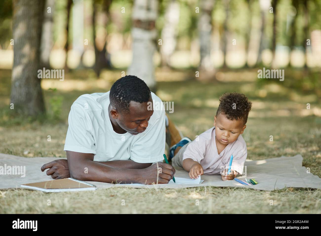 Ritratto del giovane padre afroamericano che gioca con il figlio carino nel parco mentre si posa su erba, spazio copia Foto Stock
