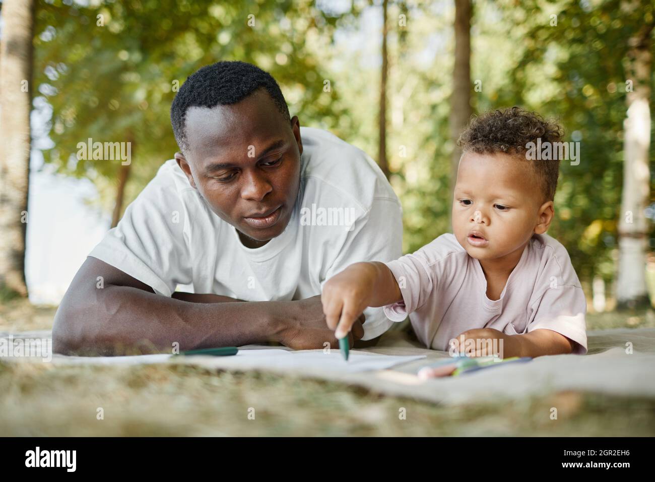 Ritratto della vista frontale del giovane padre e figlio afro-americano nel parco mentre si stendono insieme sull'erba Foto Stock