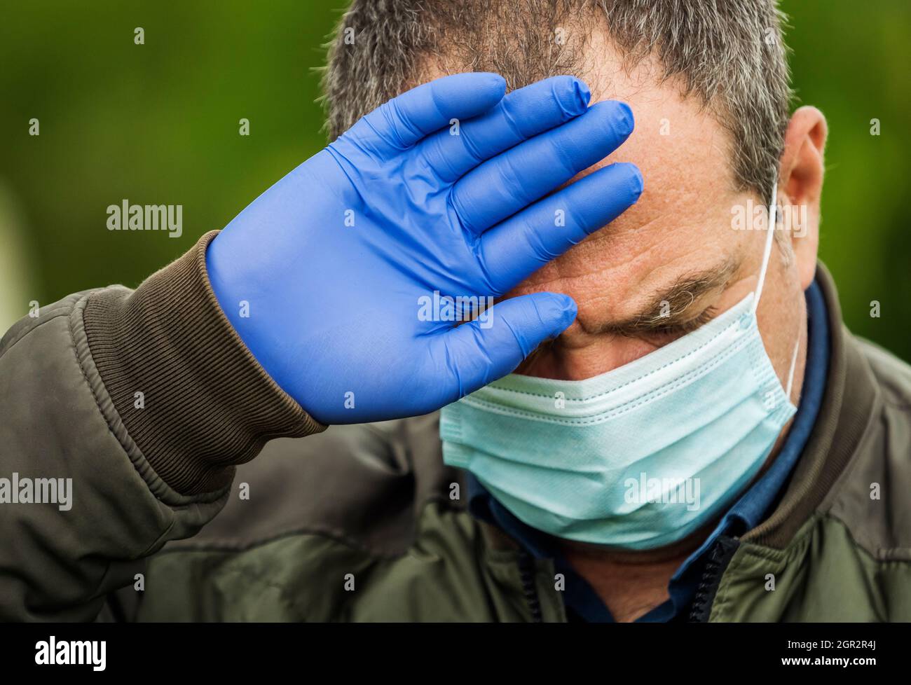 Uomo adulto in una maschera medica. Ha un mal di testa e una febbre alta. Concetto di coronavirus Foto Stock