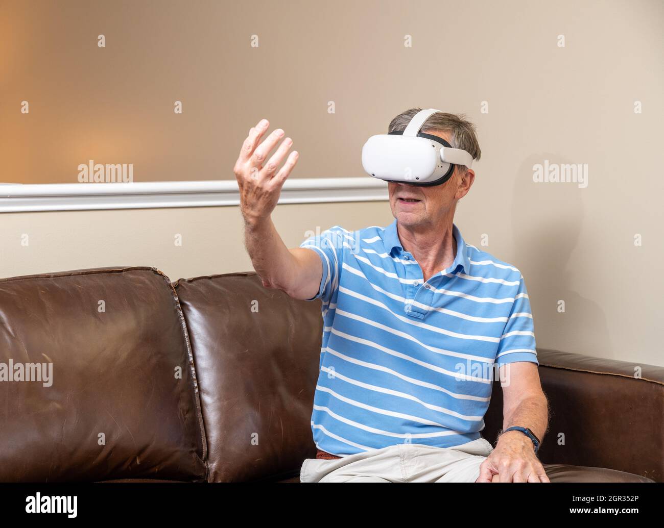 Uomo anziano che raggiunge l'oggetto su un moderno visore VR per realtà virtuale a casa Foto Stock