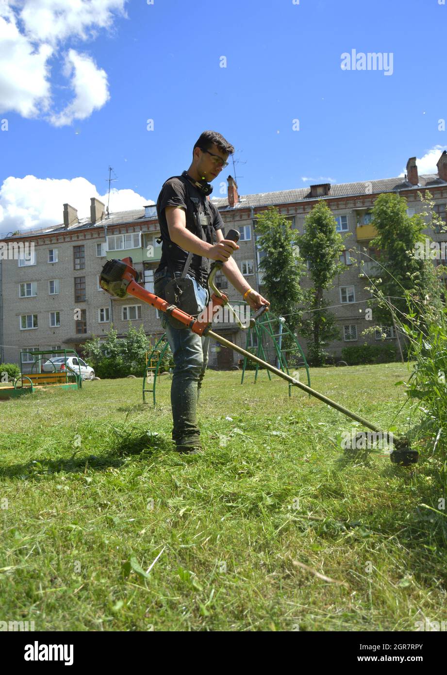 Kovrov, Russia. 28 giugno 2017. Il più giovane taglia l'erba con un trimmer per erbacce a benzina nel cortile con un edificio a cinque piani Foto Stock