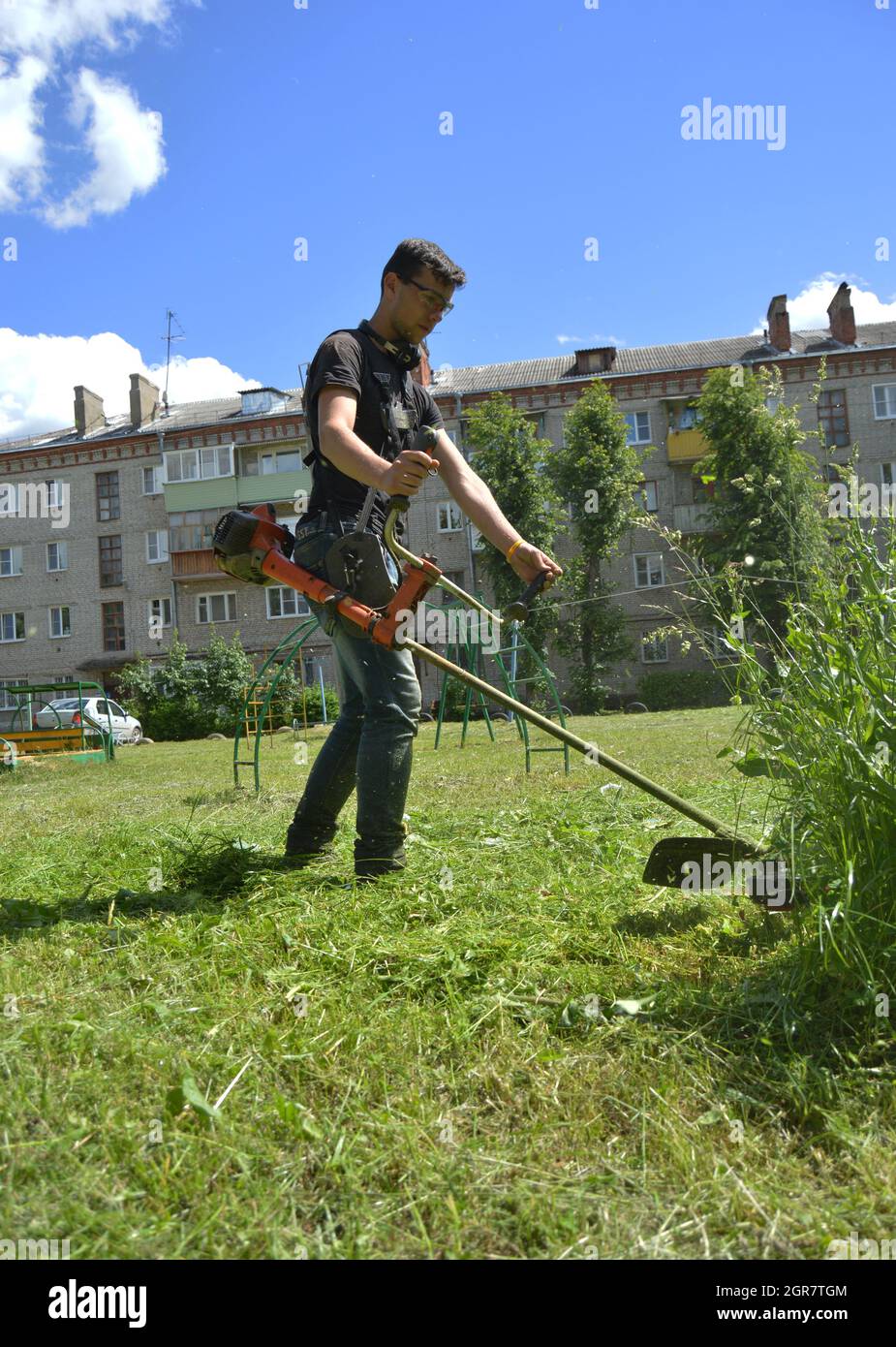 Kovrov, Russia. 28 giugno 2017. Il più giovane taglia l'erba con un trimmer per erbacce a benzina nel cortile con un edificio a cinque piani Foto Stock