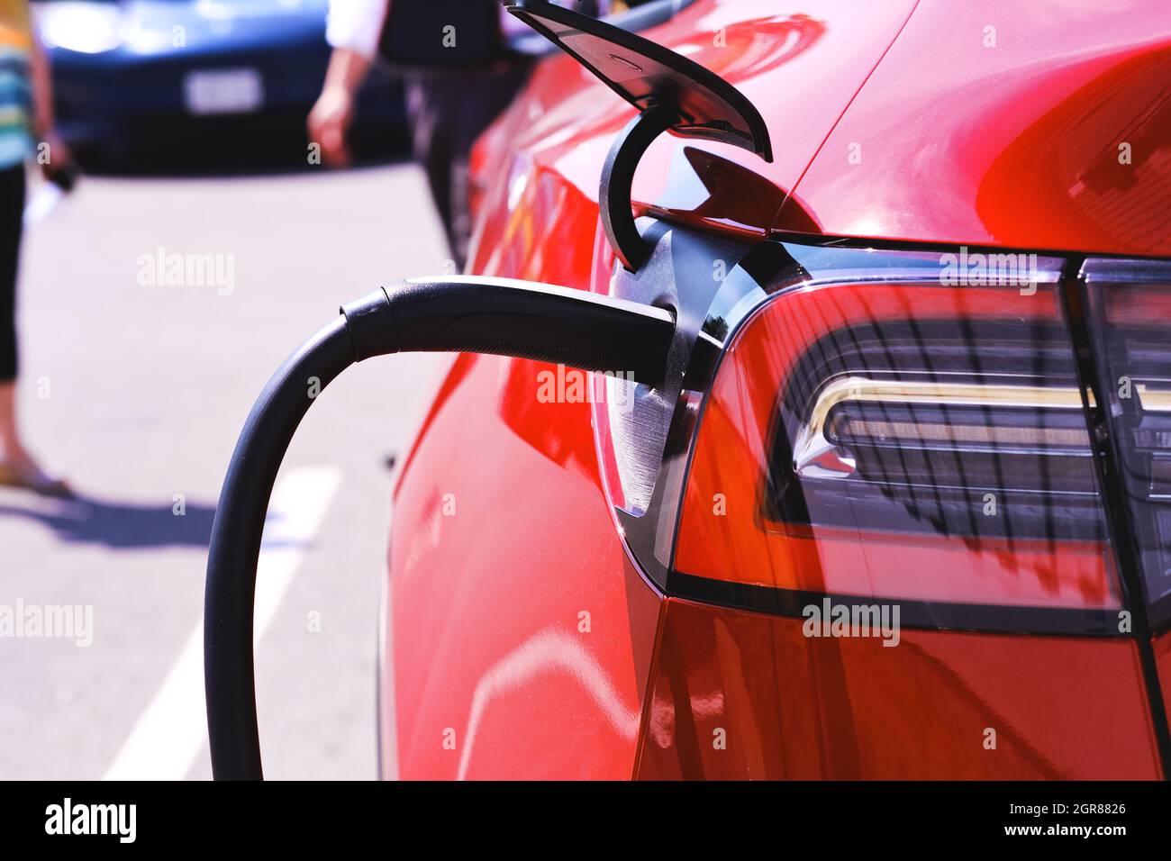 Ricarica di auto elettriche Red Tesla presso la concessionaria. Le vendite mostrano la vettura nuova al cliente nel parcheggio in background. Foto Stock