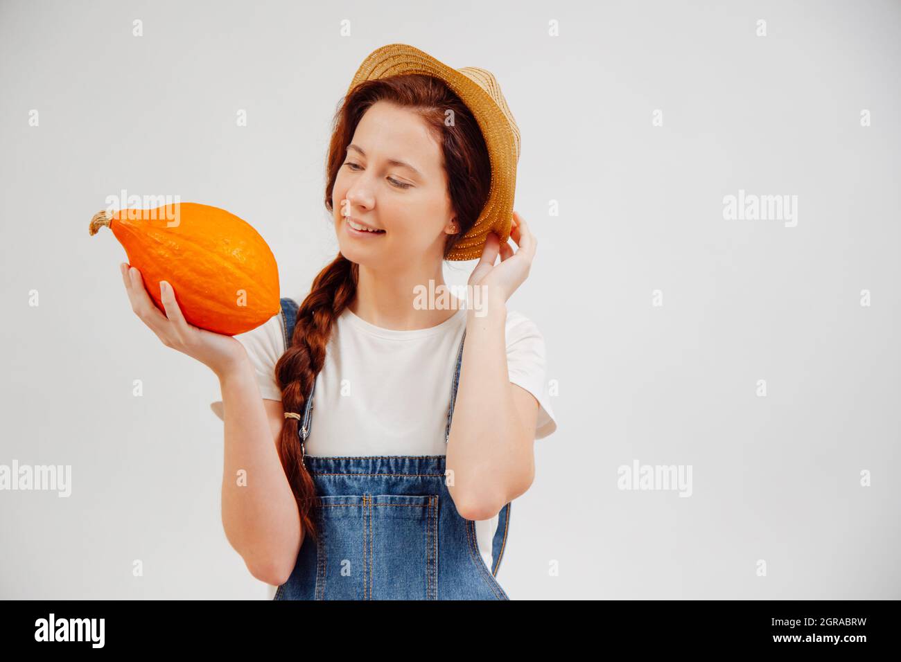 Donna contadina sorride e tiene una zucca di raccolto su uno sfondo bianco. Foto Stock