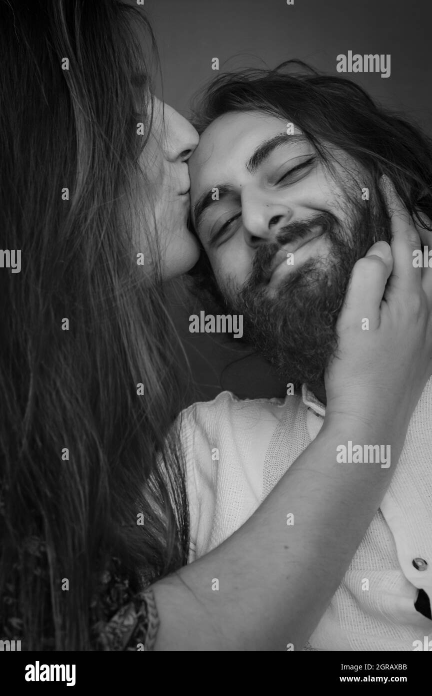Ritratto bianco e nero di una giovane coppia dove una donna dai capelli lunghi bacia la fronte dell'uomo mentre gli strizza la barba Foto Stock