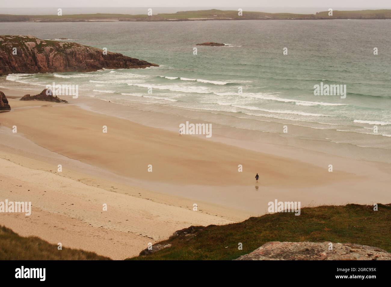 Una vista che guarda attraverso la spiaggia di Traigh Allt Chailgeag, Sutherland, Scozia, con due persone separate che camminano lungo Foto Stock