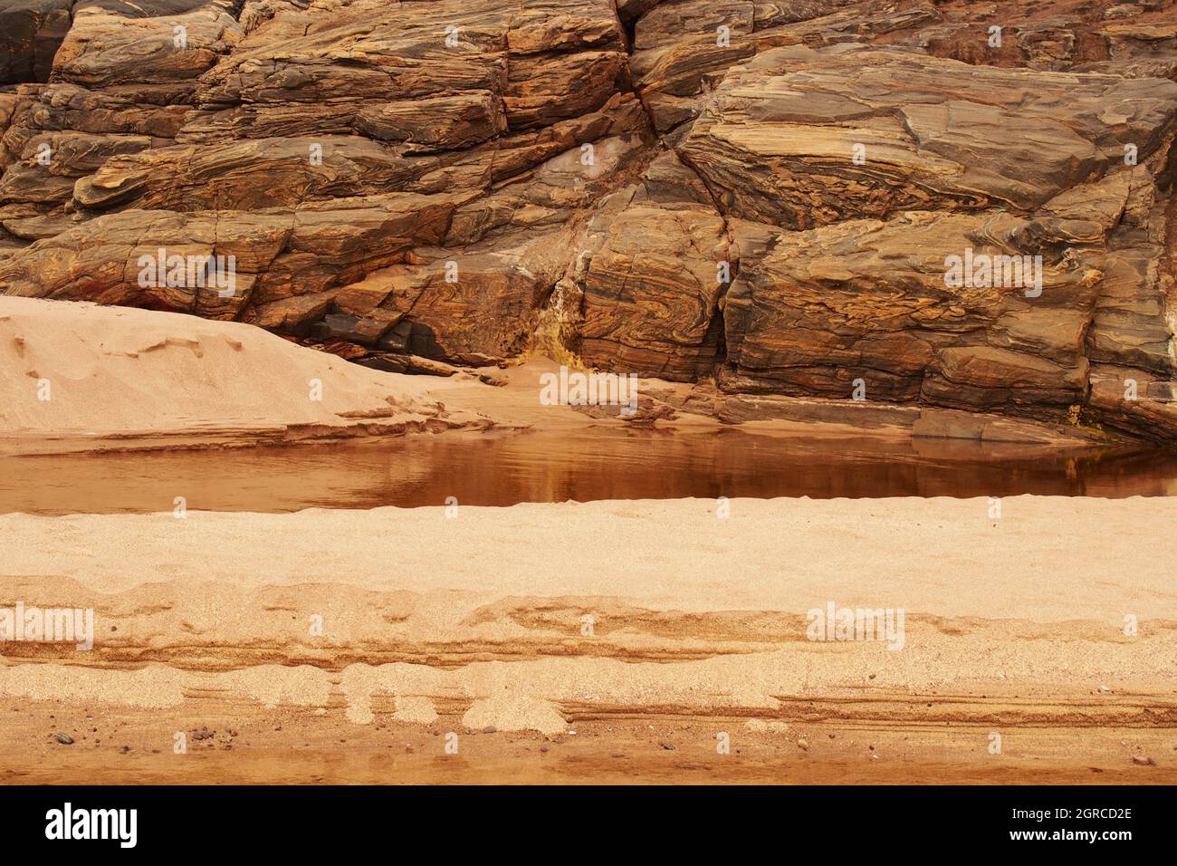 Strutture naturali di roccia e sabbia nella baia di Sandwood, Sutherland, Scozia, dove un fiume entra sulla spiaggia mostrando la roccia dei gneiss di Lewisian Foto Stock
